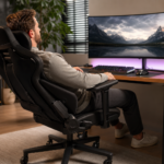 Homem sentado em uma cadeira ergonômica diante de um monitor ultrawide com paisagem de montanhas